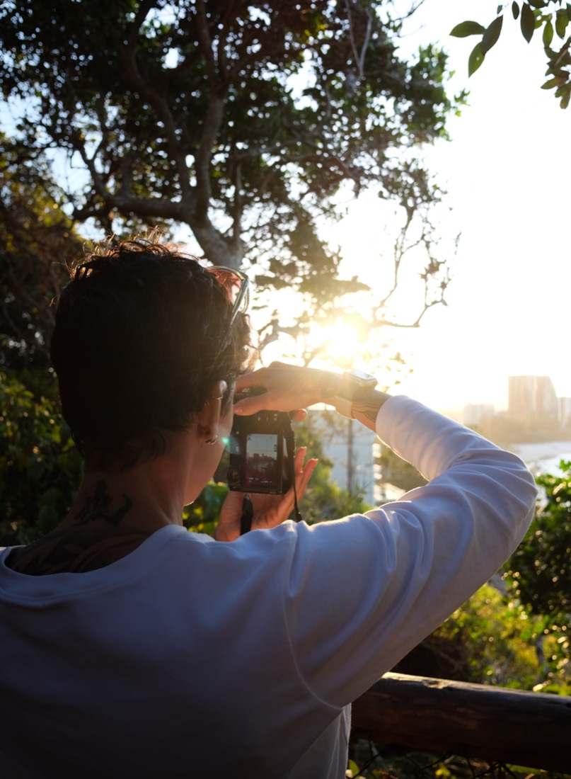A student photographing into the sunset through trees, the frame visible on the camera screen