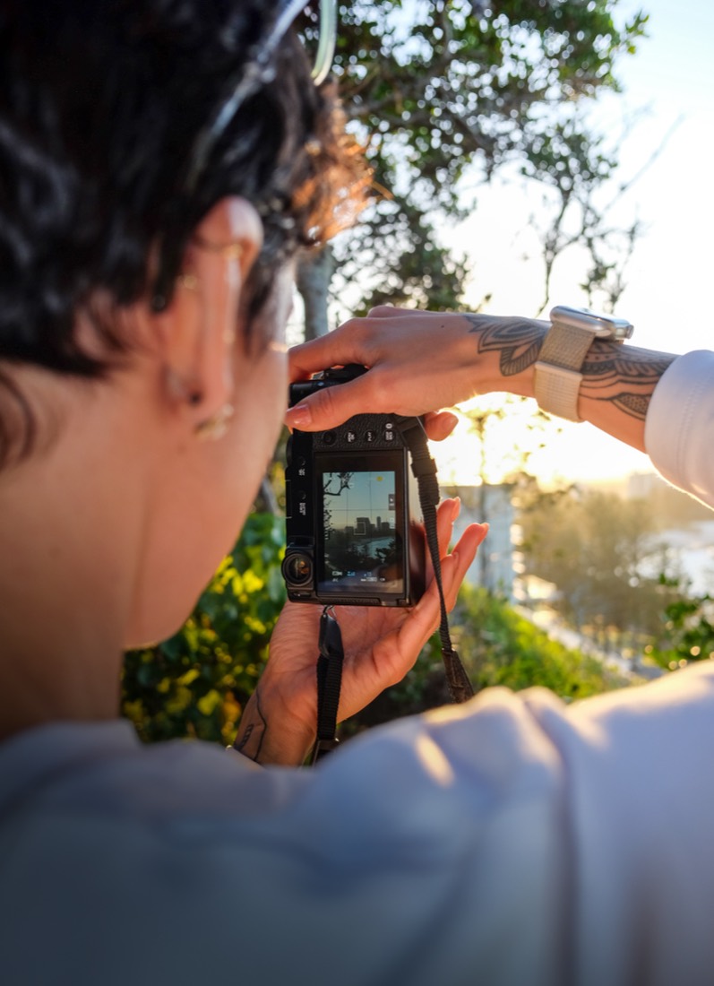 Close over a student's shoulder as they compose a shot, the scene showing on the camera's screen