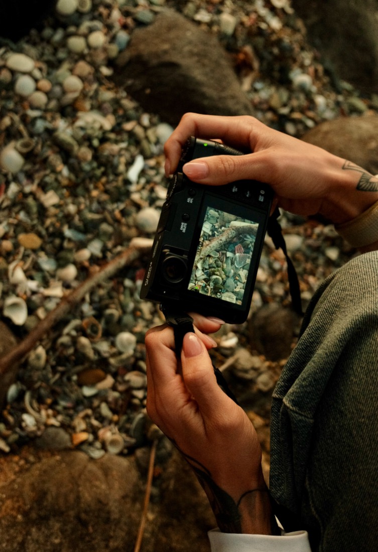 Looking down at a camera screen framing shells and pebbles on the shore