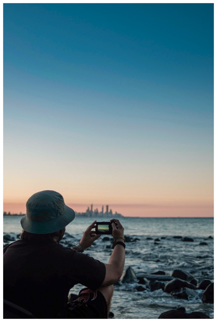 A student at the water's edge photographing the Gold Coast skyline at dusk